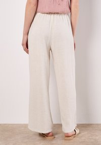 Weiße Leinen-Hosen mit weitem Bein und elastischem Bund. Der Stoff hat eine strukturierte Oberfläche. Kombiniert mit Sandalen in neutralen Farbtönen.