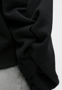 Μαύρο πουλόβερ με μαλακό, υφασμάτινο ύφασμα. Διαθέτει φουσκωτά, ραμμένα μανίκια. Κομμένο στον καρπό, σε συνδυασμό με γκρι τζιν.