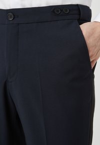Pantaloni blu realizzati in tessuto liscio, con fronte piatto, due bottoni in vita e tasche laterali. Vestibilità slim con linee pulite.