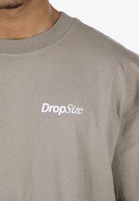Szürke pamut póló, kerek nyakkal és rövid ujjakkal, bal oldalon fehér "DropSize" logóval. Sima tapintású.