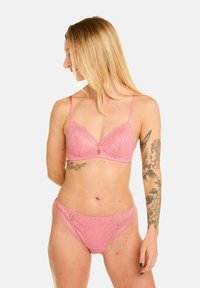 Ensemble de lingerie en dentelle rose comprenant un bralette à coques moulées et bords festonnés, ainsi que des culottes assorties avec un motif floral et une finition délicate.