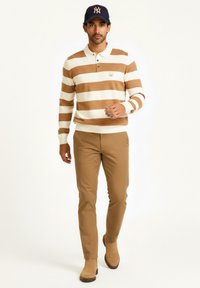 Suéter a rayas en crema y marrón, con un cuello polo, combinado con pantalones beige y botas ankle marrones, completado con una gorra oscura.