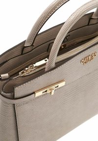 Sac à main en cuir synthétique gris avec une surface texturée, des ferrures dorées, deux anses et une fermeture zippée sécurisée.