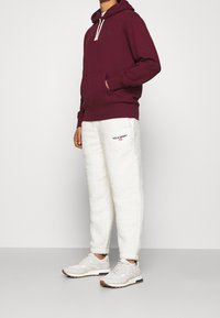 Vinröd huvtröja, vita fluffiga mjukisbyxor med texten "POLO SPORT" och ljusa sneakers med brun sula. Avslappnad och ledig passform.