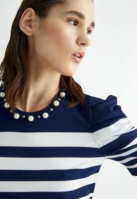 Top a righe blu navy e bianche con scollatura rotonda decorata con perle e accenti di strass e dettaglio delle spalle arricciato.