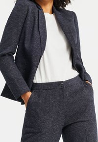  marinblå blazer i texturerad tyg med subtila fläckar, kombinerad med en vit t-shirt med rund halsringning. Skräddarsydd passform med praktiska fickor och knappstängning.