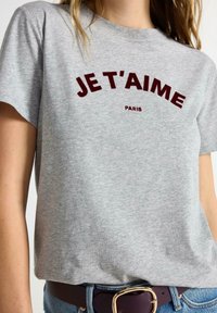 Grå bomulds t-shirt med mørkerøde tekster der står "JE T'AIME" og "PARIS." Korte ærmer, rund halsudskæring, afslappet pasform.