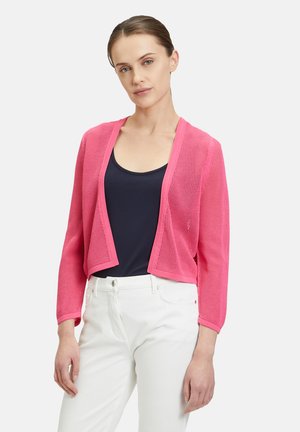Rosa transparente Strickjacke mit langen Ärmeln und offenem Vorderteil, strukturierter Strickstoff, kombiniert mit einem navyblauen Oberteil und weißen Hosen.