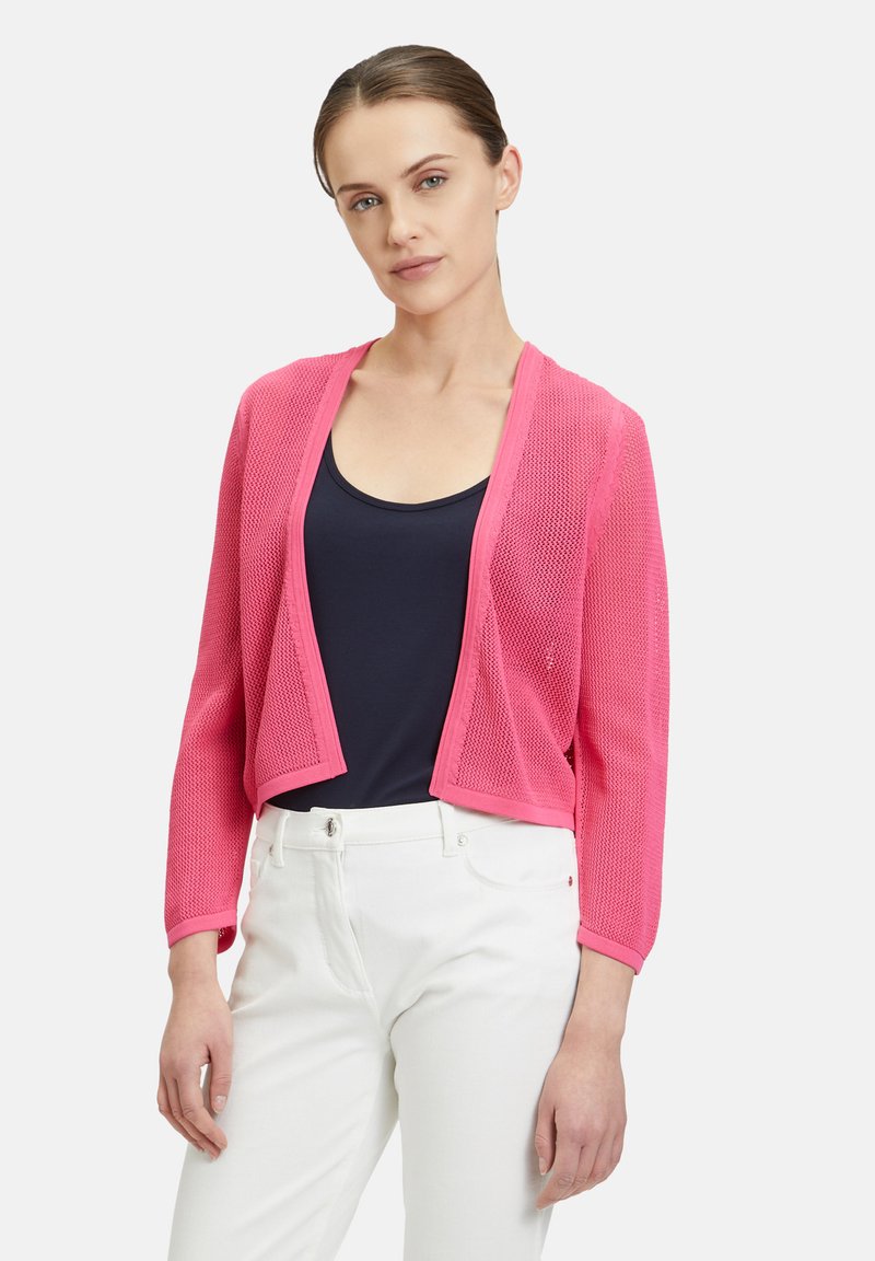 Pink sheer cardigan with long sleeves and open front, textured knit material, paired with a navy top and white pants.