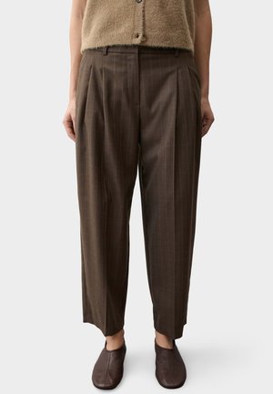 Pantalon large marron à carreaux porté avec des chaussures marron à enfiler et un haut beige sans manches en maille duveteuse.