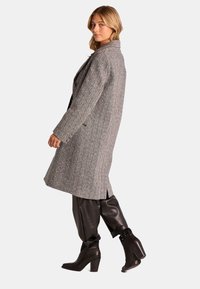 Abrigo gris de patrón de pied de poule con cuello de muesca, aberturas laterales y un corte relajado. Combinado con pantalones de cuero negro y botas de tacón grueso.