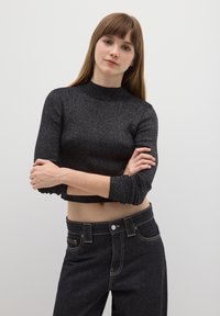 Schwarzer, kurz geschnittener Pullover mit hohem Kragen und gerippter Textur; getragen zu dunkelblauen Jeans mit kontrastierender Naht.