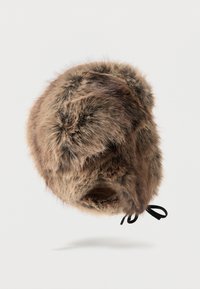 Καφέ χνουδωτό καπέλο παγίδα με αυτιά και μαύρα κορδόνια που κρέμονται σε λευκό φόντο.