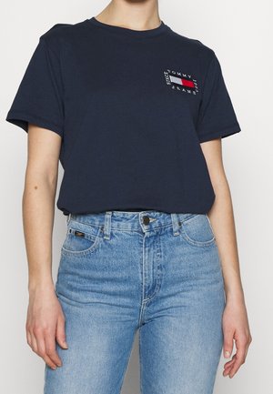 Granatowy bawełniany t-shirt z krótkimi rękawami, z małym logo w kolorach czerwonym, białym i niebieskim na lewej piersi. Do tego jasnoniebieskie dżinsy.