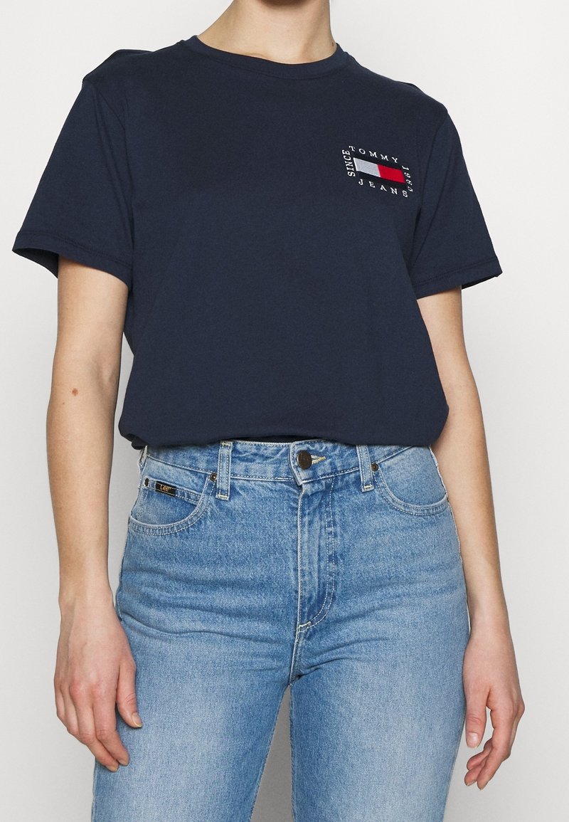 Laivastonsininen puuvillainen lyhythihainen t-paita, jossa vasemmassa rinnassa pieni punainen, valkoinen ja sininen logo. Yhdistetty vaaleansinisiin farkkuihin.