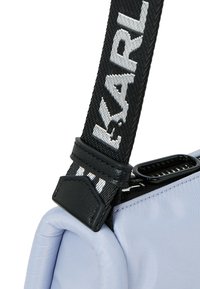 Ljusblå nylonväska med ett svart band. Bandet har texten "KARL" i vitt. Har svarta läderdetaljer och dragkedjestängning.