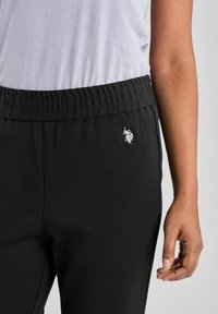 Svarta sweatpants med resårmidja, sidofickor och en liten vit logotyp. Tyget ser mjukt ut med en slät yta.