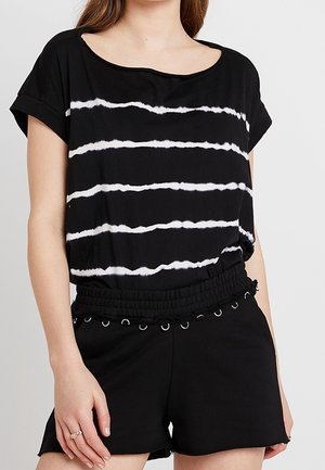 Černé tričko s bílými horizontálními pruhy, širokým výstřihem a krátkými rukávy. V kombinaci s černými kraťasy, které mají nařasený pas a kovové akcenty.