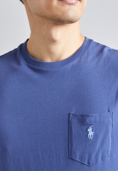 T-shirt de gola redonda em algodão azul royal sólido, com um bolso no peito esquerdo e um pequeno logótipo bordado. Textura suave, mangas curtas.
