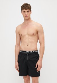 Fekete fürdőnadrág elasztikus derékkal, fehér "JACK & JONES" logóval, hálós béléssel és állítható zsinórral.