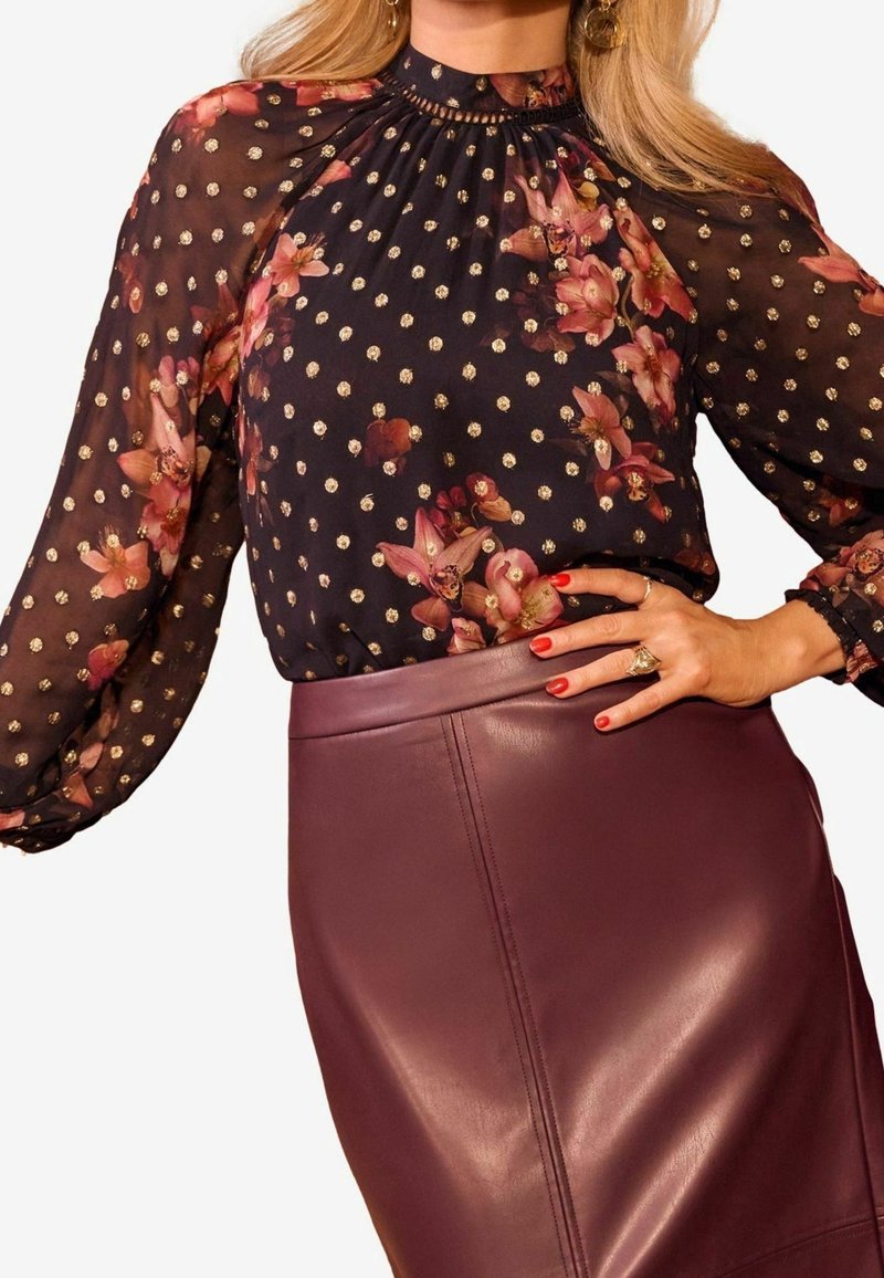 Svart blommig blus med goldiga prickar, veckad halsringning och genomskinliga långärmar, ihop med en figurnära bordeaux läderkjol.