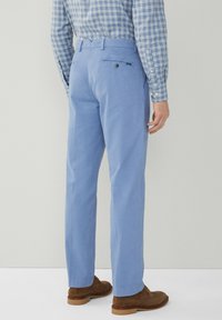 Pantaloni azzurri chiari con taglio dritto, realizzati in cotone. Presentano una tasca posteriore con bottone e passanti per cintura, abbinati a calzature marroni.