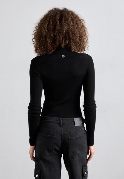 Pull col montant noir à côtes avec des manches longues, associé à un pantalon cargo noir avec poches plaquées et une étiquette en cuir de marque.