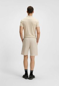 Polo beige con texture a motivo sottile, abbinato a pantaloni beige. Completato con calze nere con scritte bianche e scarpe nere.