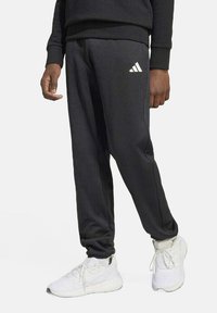 Zwarte Adidas sweatpants met een elastische tailleband, taps toelopende pijpen en een wit logo op de linkerheup, gecombineerd met witte sport sneakers.