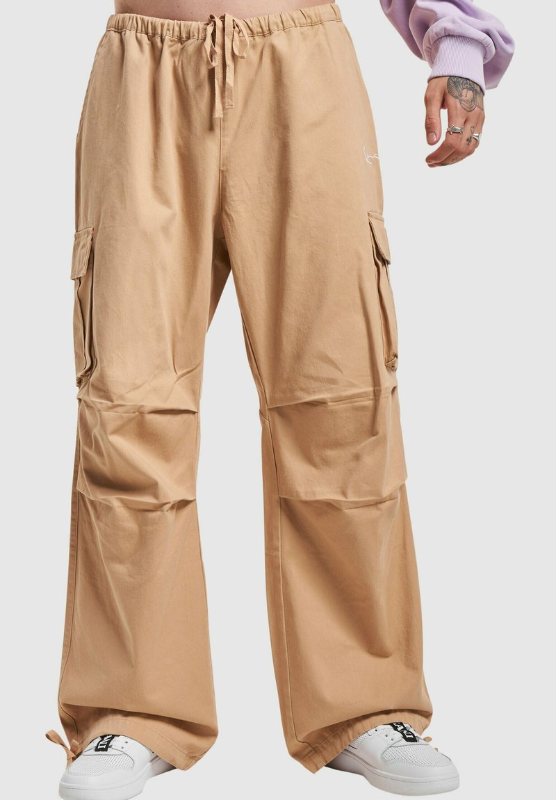 Beige cargo bukser med elastisk talje og snor, med to sidelommer og løs pasform. Båret med hvide sneakers.