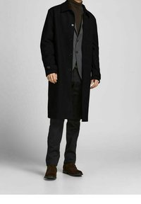 Svart ylleöverrock med krage, knappstängning och sidofickor, lager på lager över en grå väst och mörka byxor, matchat med bruna skor.