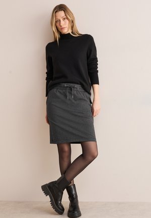 Pull noir et jupe grise à cordon, associés à des bottines noires. Tissu texturé, finition lisse, design près du corps et longueur genou.