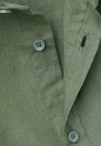 Tela de camisa verde oliva con una textura suave, que presenta un cierre de botón con un botón azul claro y un pequeño ojal.