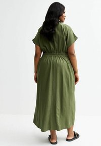 Olivgrünes, knöchellanges Kleid mit Elastikbund, kurzen Ärmeln und lockerer Passform. Hergestellt aus leichtem Stoff.
