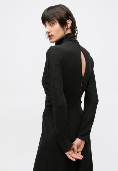 Fekete, hosszú ujjú ruha magas nyakkal és nyitott hátú kialakítással. Texturált anyag; testhez álló derék, ami szabályosan bő szoknyába torkollik.