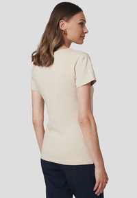 Beżowa bawełniana koszulka z krótkim rękawem, okrągłym dekoltem i luźnym krojem, charakteryzująca się gładką teksturą i minimalistycznym designem.