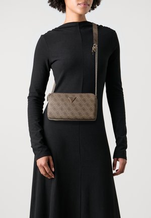 Borsa a tracolla marrone con motivo e strap in catena, con dettaglio del logo triangolare, indossata da una persona in un lungo abito nero.