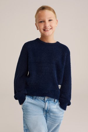 Suéter de punto azul marino con una textura suave, cuello redondo y puños enrollados, combinado con jeans de mezclilla azul claro.