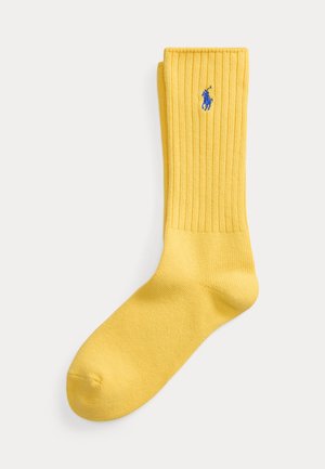 Une chaussette côtelée jaune unique avec un petit logo brodé d'un joueur de polo bleu près du haut de la manchette.