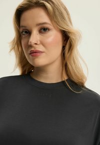 Czarna bluza z okrągłym dekoltem i subtelnym wytłoczonym logo na klatce piersiowej. Miękki bawełniany materiał o gładkiej teksturze.