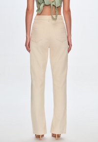 Jeans de tiro alto en color beige, con corte ancho y textura suave, dos bolsillos traseros y un ligero acampanado en el dobladillo.