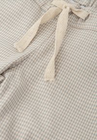 Tela de color azul claro y beige con un sutil diseño de pata de gallo. Presenta un cordón beige con extremos deshilachados. Textura suave.