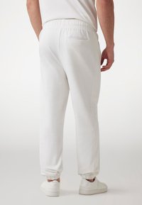 Hvide joggere lavet af blødt materiale med en elastisk talje, ribbede manschetter og en baglomme med et struktureret sidepanel.