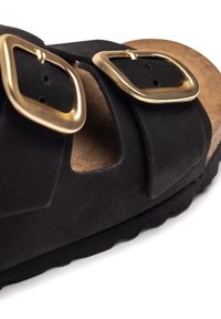 Sandal in suede nera con due cinturini larghi e fibbie quadrate dorate, e una soletta in cuoio testurizzato marrone. Suola in gomma con bordo ondulato.