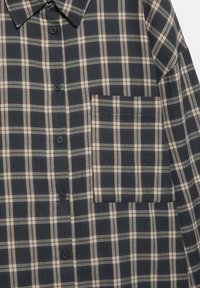 Cămașă în carouri de culoare bleu închis și bej. Design cu închidere prin nasturi, guler clasic și un singur buzunar pe piept. Textură moale a materialului, croială lejeră.