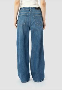 Jean en denim foncé à jambes larges et taille haute. Dispose de deux poches arrière et d'une finition nette au niveau de l'ourlet. Le tissu semble doux.