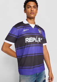 Sort og lilla stribet fodboldtrøje med hvid krave, der har "REPLAY FC" logo i fed hvid tekst og et skjoldemblem på brystet.
