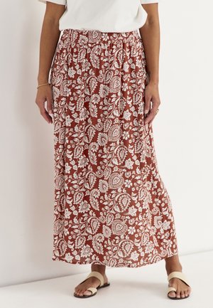 Brun maxinederdel med hvide blomster- og paisleymønstre, båret med en hvid top og beige flade sandaler, vist fra taljen til fødderne.