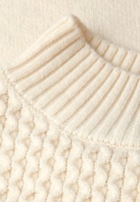 Off-white stickad tröja med en ribbad hög krage och en texturerad kropp med ett bubblande mönster. Mjuk, tjockt tyg är synligt.