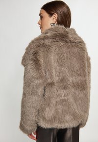 Brun faux fur jakke med en tekstureret, fluffy overflade, der har en høj krave og lange ærmer, vist fra bagsiden.